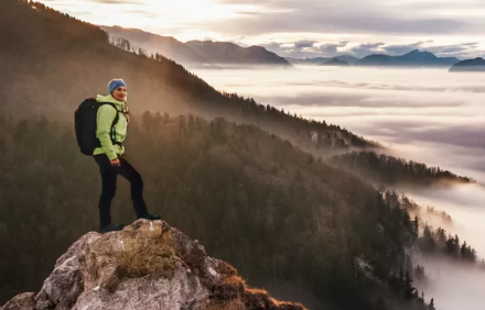 Une femme au sommet d'une montagne avec vue sur la vallée et les nuages.
