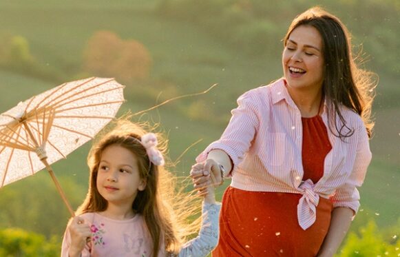 Une famille marchant dans un paysage avec la femme enceinte, la fille tenant un parapluie et le père un cerf volant.